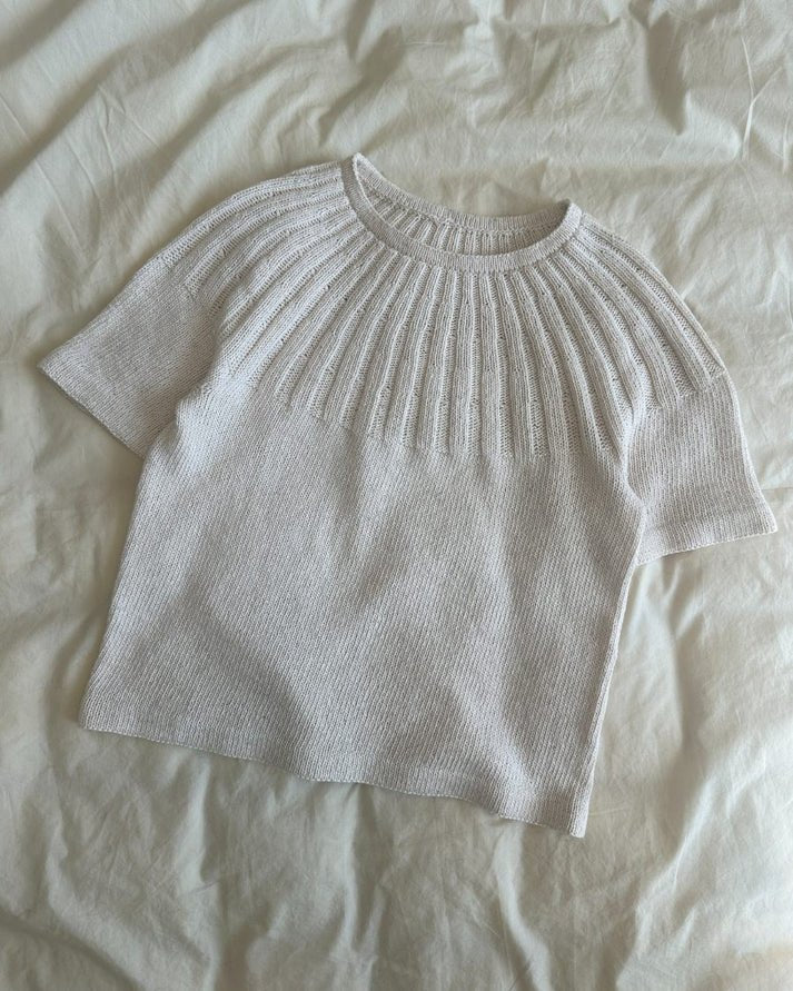 Sunday Tee on siro, naisellinen ja ajattoman kaunis lyhythihainen neulepaita, jota koristaa näyttävä ja joustava pyöreä joustinneulekaarroke.