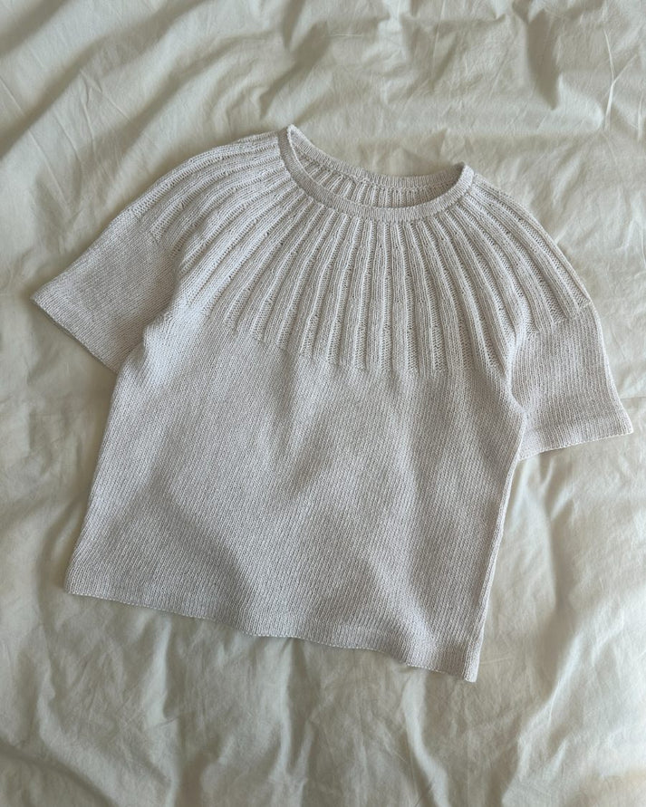 Sunday Tee on siro, naisellinen ja ajattoman kaunis lyhythihainen neulepaita, jota koristaa näyttävä ja joustava pyöreä joustinneulekaarroke.
