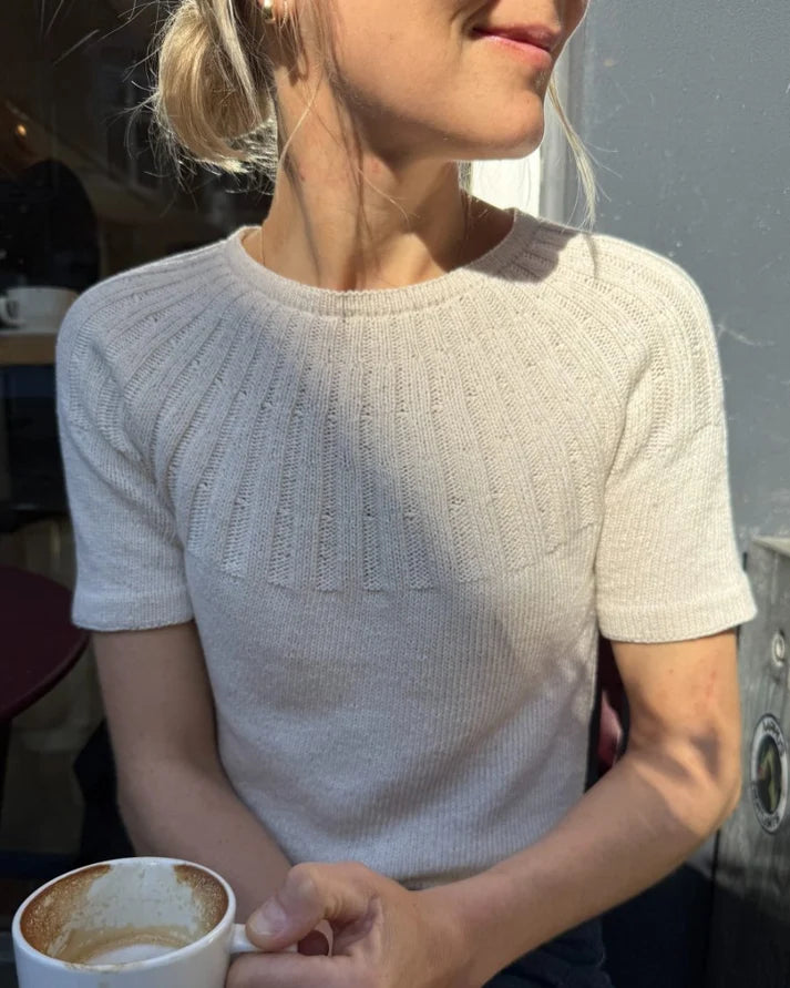 Sunday Tee on siro, naisellinen ja ajattoman kaunis lyhythihainen neulepaita, jota koristaa näyttävä ja joustava pyöreä joustinneulekaarroke.